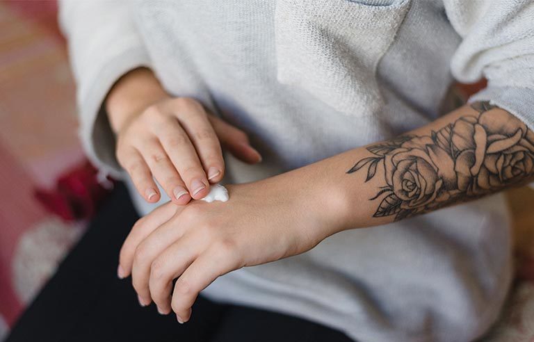 person applying tattoo aftercare cream to newly tattooed skin