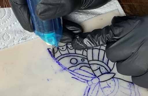 tattoo artist tattooing a straight line on fake skin